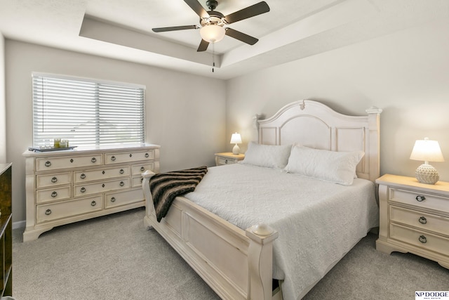 bedroom with a ceiling fan, a tray ceiling, and light colored carpet