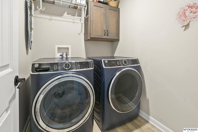 washroom featuring cabinet space, baseboards, washing machine and dryer, and light wood-style flooring