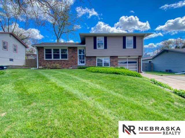 tri-level home featuring an attached garage, a front lawn, driveway, and brick siding