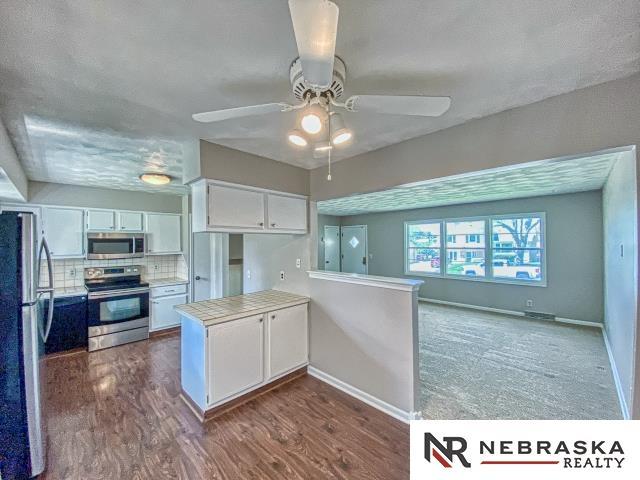 kitchen featuring appliances with stainless steel finishes, white cabinetry, a ceiling fan, baseboards, and a peninsula