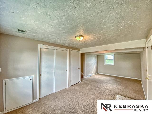 unfurnished bedroom featuring a textured ceiling, visible vents, baseboards, two closets, and carpet