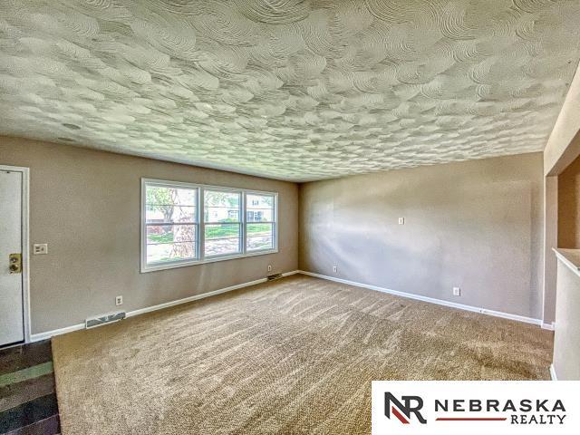 empty room featuring carpet flooring, a textured ceiling, visible vents, and baseboards