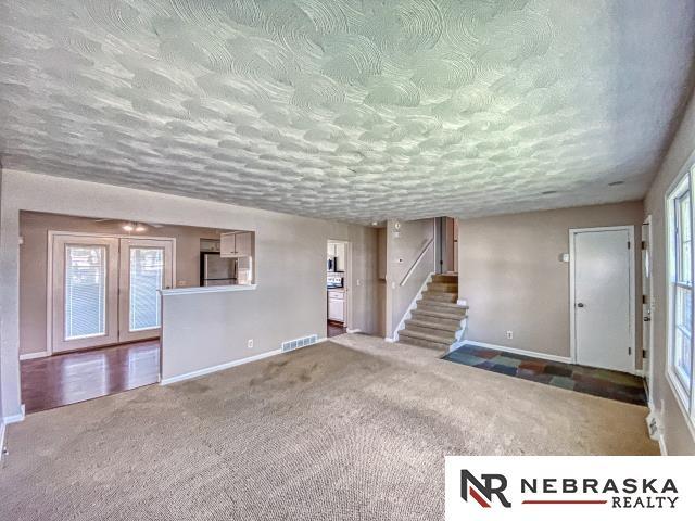 unfurnished living room featuring carpet floors, visible vents, stairs, baseboards, and a textured ceiling