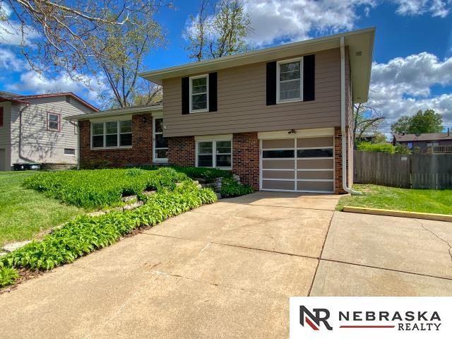tri-level home featuring a garage, fence, driveway, and brick siding