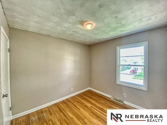 spare room featuring baseboards, a textured ceiling, wood finished floors, and visible vents