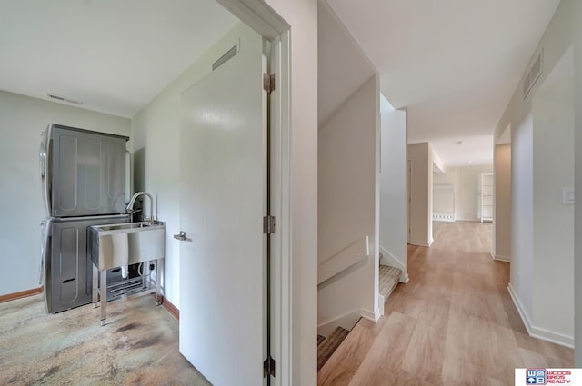 hallway with visible vents, stacked washer and clothes dryer, baseboards, and light wood-type flooring