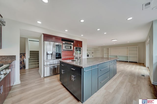 kitchen with visible vents, appliances with stainless steel finishes, a sink, light stone counters, and light wood-style floors