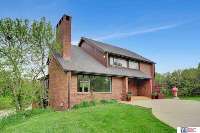 view of front of property featuring a chimney, brick siding, roof with shingles, and a front yard