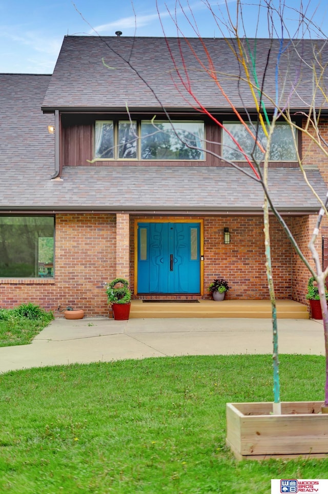 view of front of home featuring a shingled roof, a front lawn, and brick siding