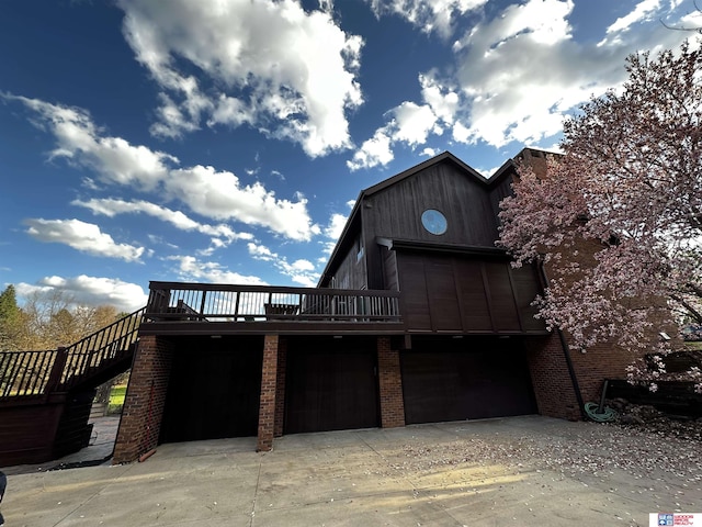 back of house featuring a wooden deck, stairs, driveway, and brick siding