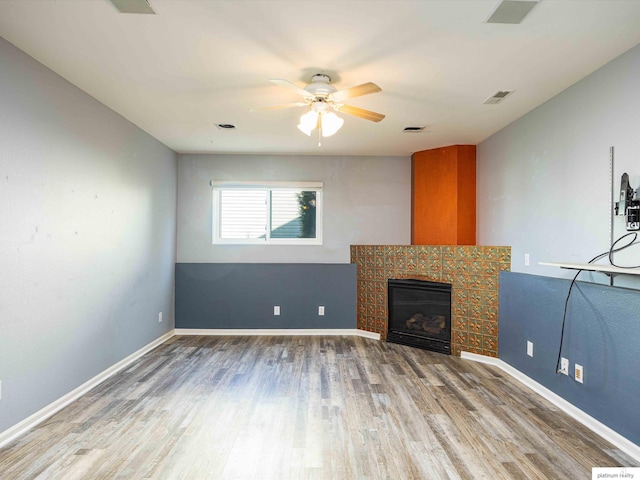 unfurnished living room featuring ceiling fan, wood finished floors, a tile fireplace, and baseboards