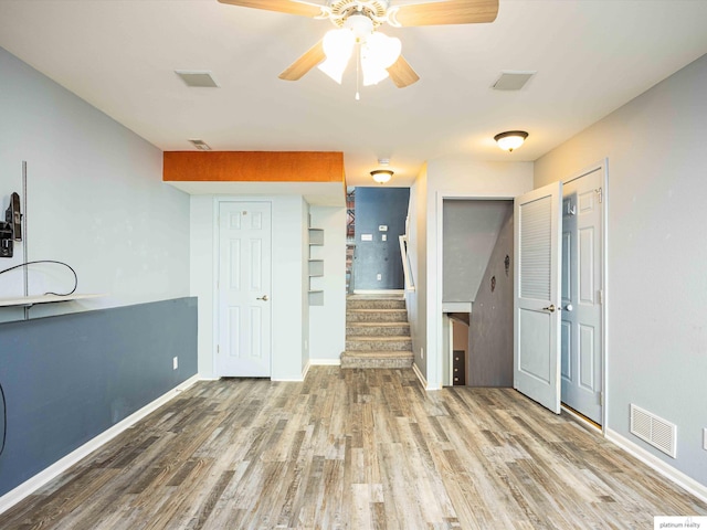 unfurnished living room featuring stairway, wood finished floors, baseboards, and a ceiling fan