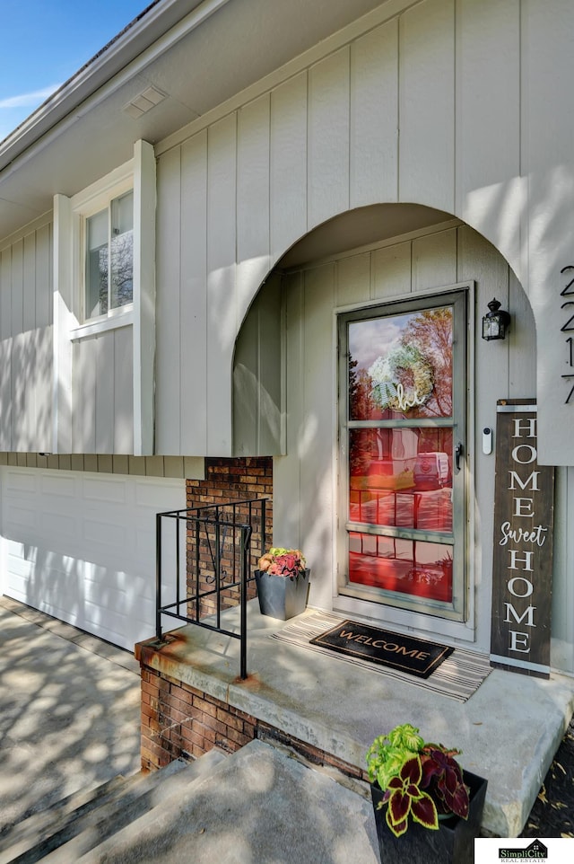property entrance with an attached garage, board and batten siding, and driveway