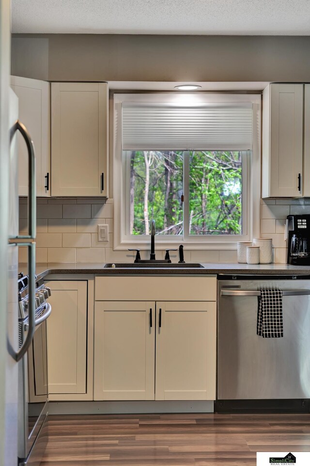 kitchen featuring wood finished floors, dark countertops, tasteful backsplash, a sink, and dishwasher