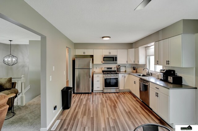 kitchen with appliances with stainless steel finishes, tasteful backsplash, light wood-type flooring, a sink, and white cabinetry