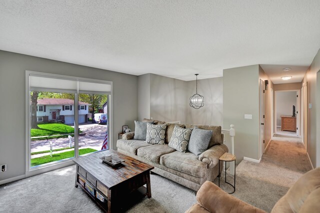 living area featuring light colored carpet, a textured ceiling, baseboards, and a notable chandelier
