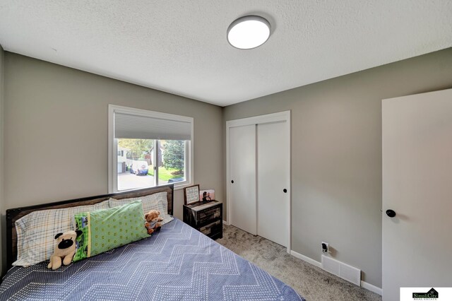 bedroom featuring a textured ceiling, visible vents, baseboards, a closet, and light carpet
