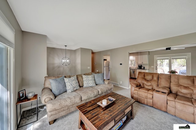 living room featuring visible vents, baseboards, ceiling fan with notable chandelier, and light carpet
