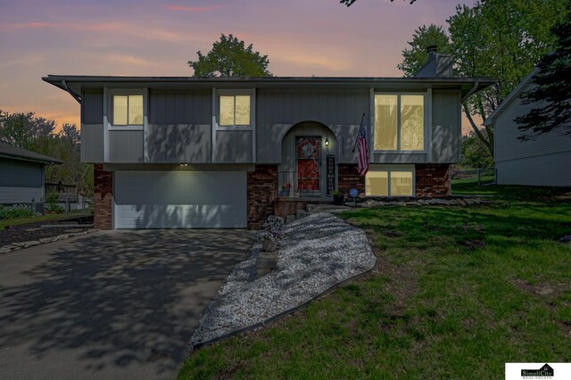 bi-level home with a garage, brick siding, and aphalt driveway
