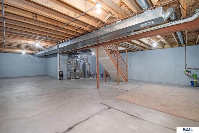 unfinished basement with stairway, heating unit, gas water heater, and concrete block wall