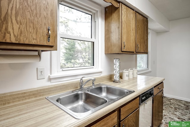 kitchen featuring a sink, dishwasher, light countertops, brown cabinetry, and a wealth of natural light