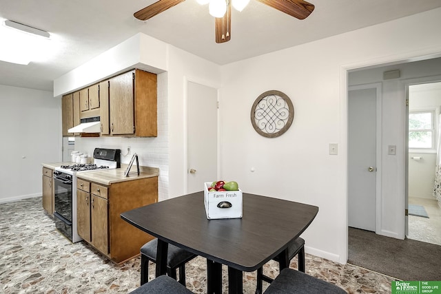 kitchen featuring brown cabinets, ceiling fan, gas stove, light countertops, and under cabinet range hood
