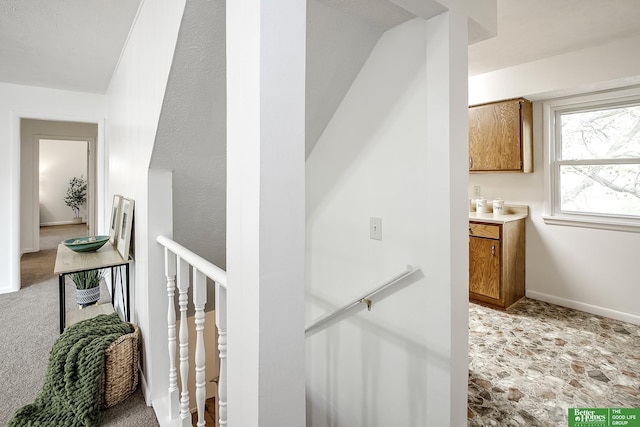 corridor featuring stone finish flooring, baseboards, and an upstairs landing