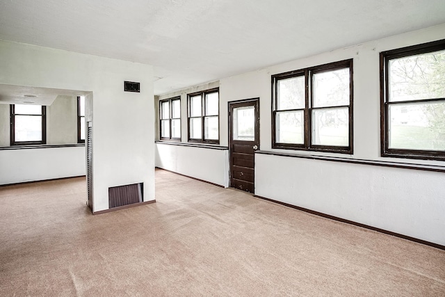 unfurnished room with light colored carpet, baseboards, and a wealth of natural light