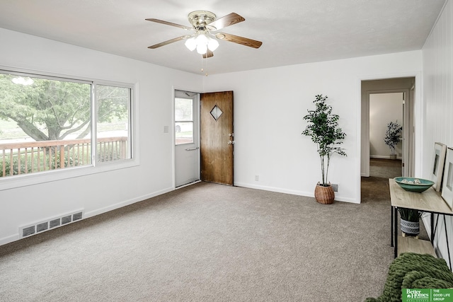 carpeted empty room with baseboards, a ceiling fan, and visible vents