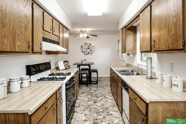 kitchen featuring ceiling fan, a sink, gas stove, stone finish floor, and under cabinet range hood
