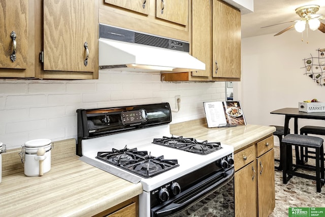 kitchen with decorative backsplash, ceiling fan, gas range, light countertops, and under cabinet range hood