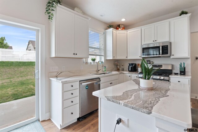kitchen with stainless steel appliances, a sink, light wood-type flooring, white cabinets, and light stone countertops