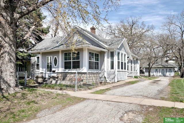 bungalow featuring a shingled roof, a chimney, an outdoor structure, and aphalt driveway