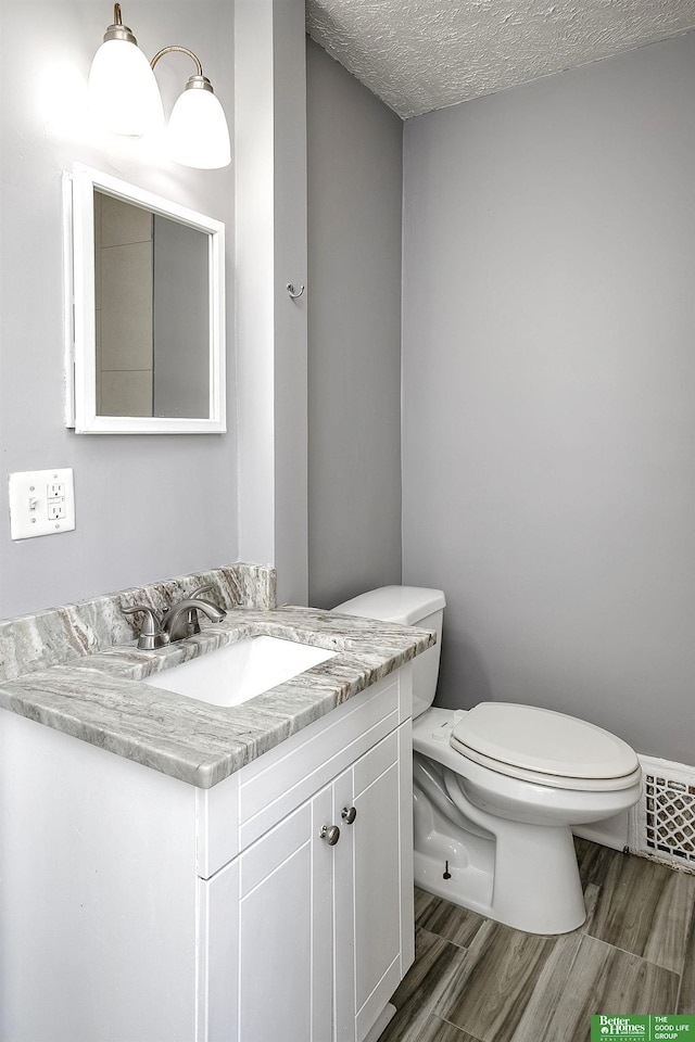 bathroom with vanity, a textured ceiling, wood finished floors, and toilet