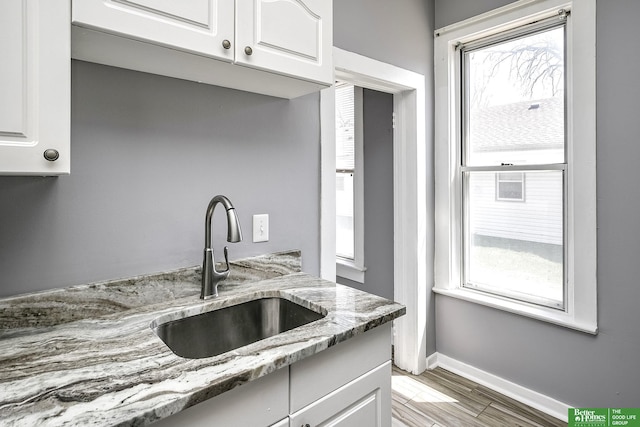 kitchen with a sink, baseboards, white cabinets, and a healthy amount of sunlight