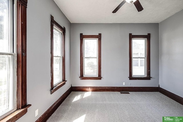 carpeted empty room featuring ceiling fan, a healthy amount of sunlight, and baseboards