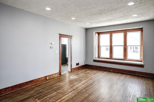 empty room with a textured ceiling, visible vents, dark wood finished floors, baseboards, and recessed lighting
