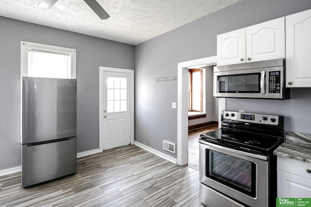 kitchen with stainless steel appliances, a textured ceiling, visible vents, and white cabinetry