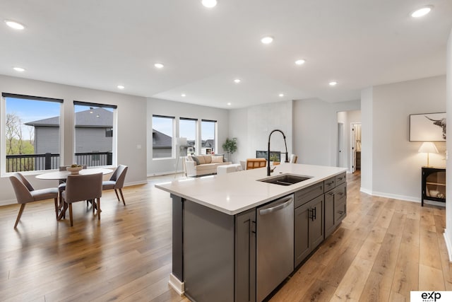 kitchen featuring a sink, dishwasher, light countertops, light wood-type flooring, and a center island with sink