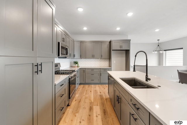 kitchen with a sink, appliances with stainless steel finishes, gray cabinetry, and light countertops