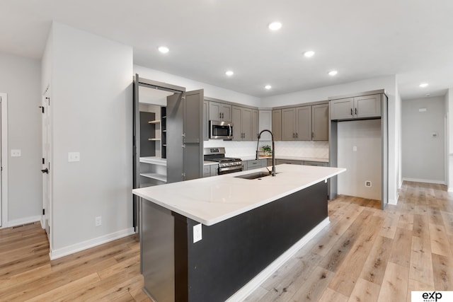 kitchen featuring a sink, light wood finished floors, gray cabinetry, and stainless steel appliances
