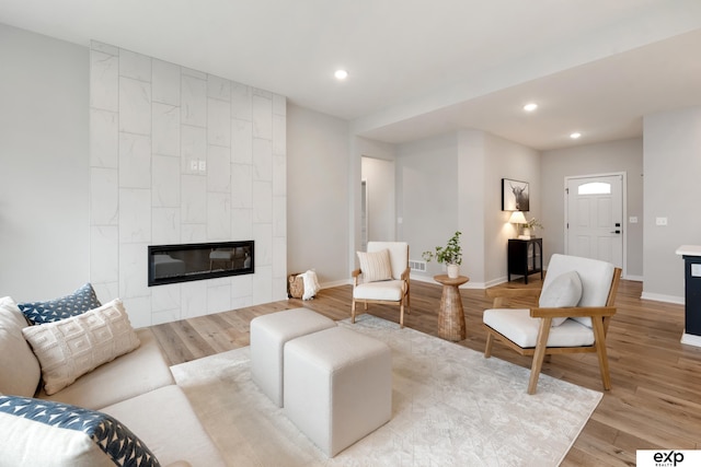 living room featuring baseboards, light wood finished floors, visible vents, and a fireplace