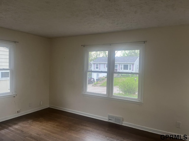 unfurnished room featuring visible vents, a textured ceiling, dark wood-type flooring, and baseboards