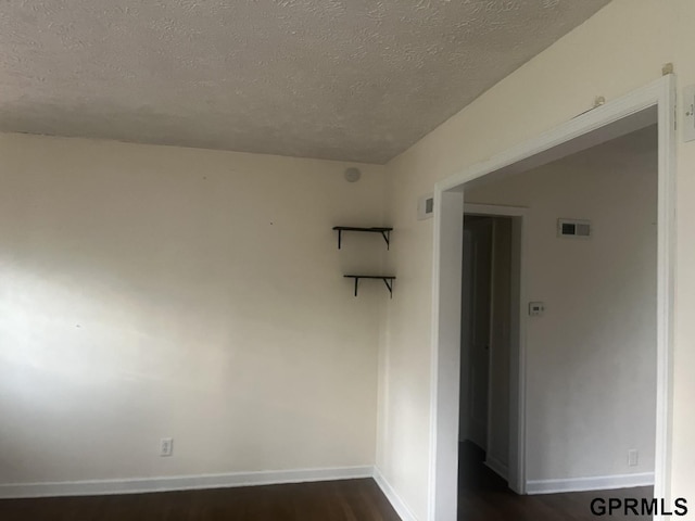 empty room featuring baseboards, dark wood-style flooring, a textured ceiling, and visible vents