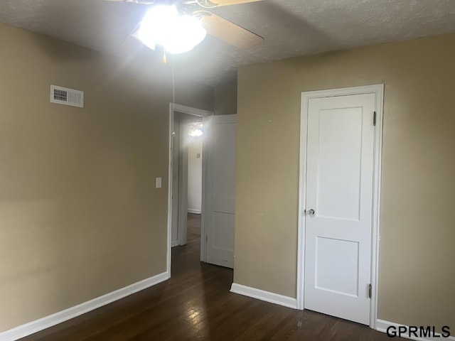 unfurnished bedroom with ceiling fan, a textured ceiling, visible vents, dark wood finished floors, and baseboards