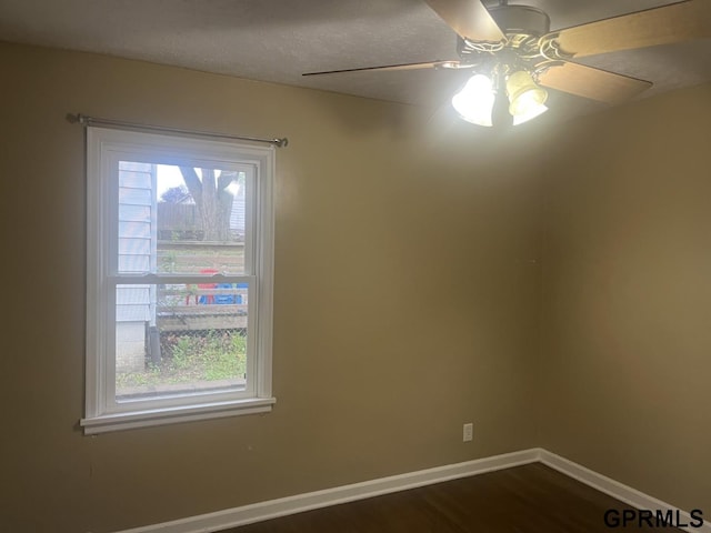 unfurnished room featuring baseboards, a ceiling fan, plenty of natural light, and dark wood-type flooring