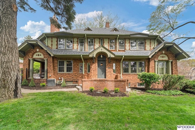 tudor home featuring brick siding, fence, a front yard, and a chimney