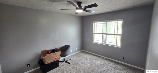 unfurnished office with carpet floors, a textured ceiling, a ceiling fan, baseboards, and visible vents