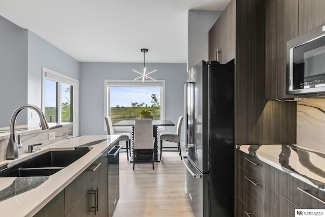 kitchen featuring modern cabinets, light stone counters, a sink, light wood-style flooring, and appliances with stainless steel finishes