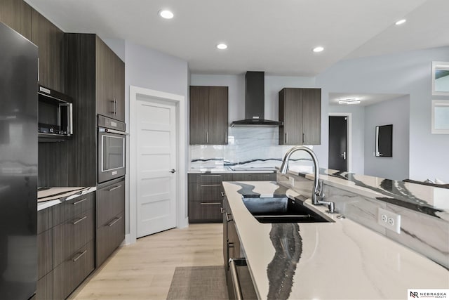 kitchen with refrigerator, stainless steel oven, modern cabinets, wall chimney exhaust hood, and a sink